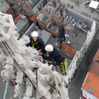 2 werkmannen op grote hoogte werken aan toren kerk
