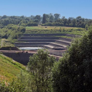 Een groen landschap onder een blauwe lucht. Op een van de hellingen is een trapsgewijze afgraving van een kleiput zichtbaar.