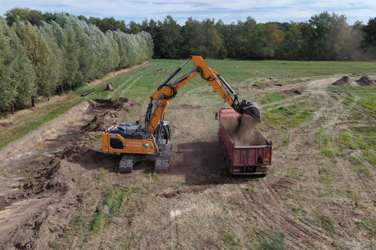 Een dronefoto van een graafmachine die aarde in de laadbak van een vrachtwagen stort. 