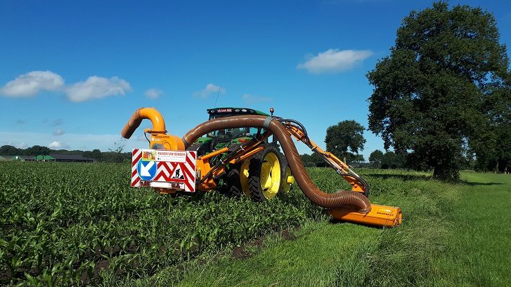 Een gespecialiseerde landbouwmachine maait de gras- en kruidenrand rond een akker.