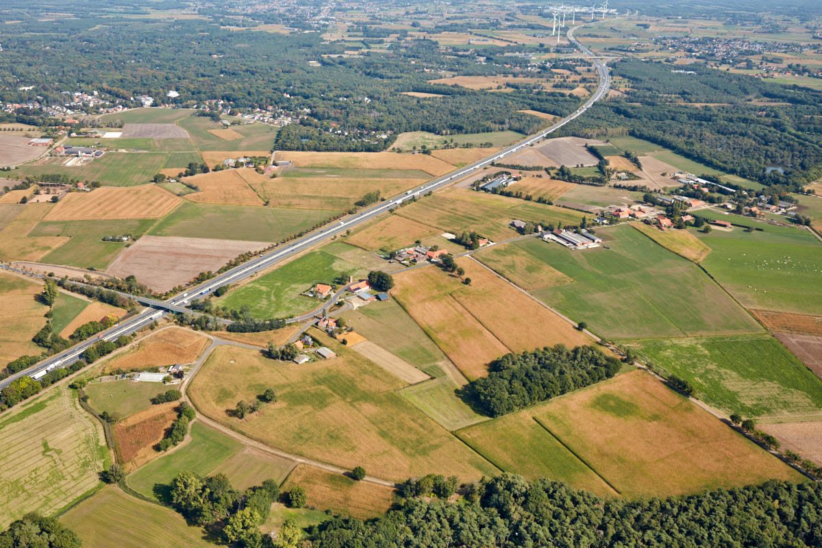 Luchtfoto van het landbouwgebied Corsendonck in Oud-Turnhout, genomen in september 2021. De foto toont vergeelde velden, enkele bosacthige gebieden, een berbindingsbaan en enkele verspreide woningen en andere gebouwen. . 