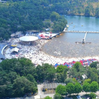 Luchtfoto: tussen de bomen ligt een meer met een strand. Tal van strand- en zwemvoorzieningen zijn zichtbaar (redderstoren, glijbanen, aanlegsteiger,...) Heel veel bezoekers zijn als kleine stipjes zichtbaar op het strand en in het water.