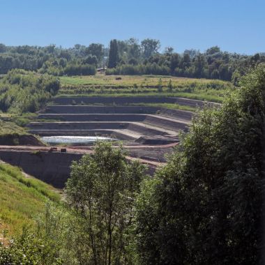Een groen landschap onder een blauwe lucht. Op een van de hellingen is een trapsgewijze afgraving van een kleiput zichtbaar.