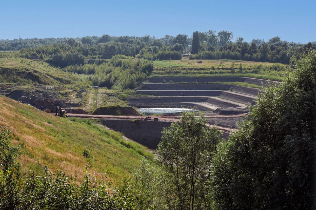 Een groen landschap onder een blauwe lucht. Op een van de hellingen is een trapsgewijze afgraving van een kleiput zichtbaar.