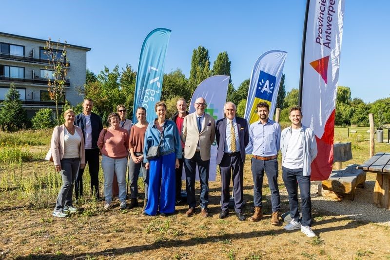 Een groep mensen poseert voor enkele beachvlaggen naast een picknickbank. 