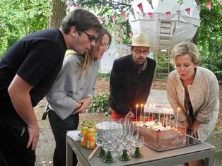 Een jong koppeltje en een man en vrouw blazen tien kaarsjes op een taart uit, op de achtergrond een bolvormige tent in een park, er hangen vlaggenslingers op. Viering 10 jaar Terra Nova in Arboretum Kalmthout.