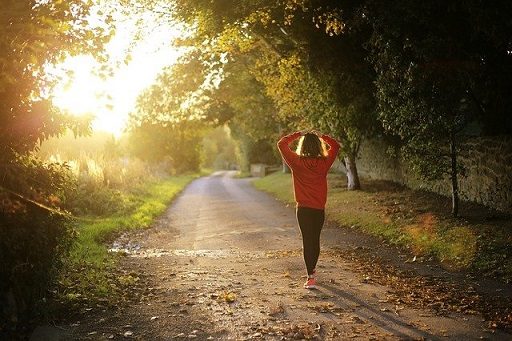 Jonge vrouw in sportieve kleding op bospad bij zonsondergang.