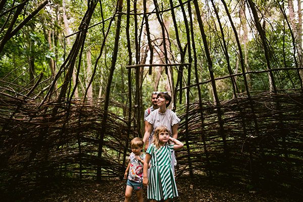 Een gezin met twee jonge kinderen gaat een wilgenhut in het Trollenbos van De Schorre in Boom binnen. Het wilgenriet is niet aansluitend, waardoor er licht binnenkomt, voornamelijk langs de bovenkant. De vrouw kijkt naar de dakconstructie boven haar dat licht doorlaat. Ze moedigt de kinderen met een klein duwtje in de rug aan om verder te wandelen, terwijl haar man achter haar volgt. De kinderen kijken vol bewondering rondom zich.